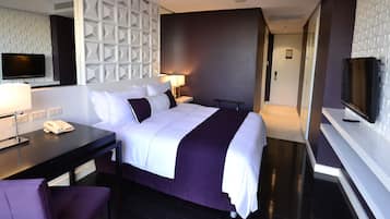 Una habitación de hotel moderna con una cama grande, un escritorio con teléfono, una silla, un televisor y un televisor de pared.