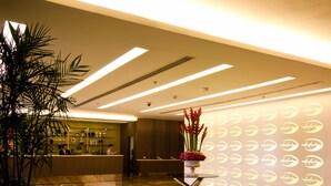 Un moderno vestíbulo de hotel con mostrador de recepción, una planta en maceta grande, un jarrón decorativo con flores y una pared con motivos circulares.