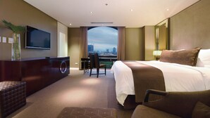 Habitación de hotel con una cama grande, un escritorio, una silla, un televisor y vistas a la ciudad.