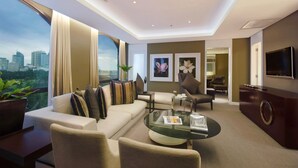 Habitación de hotel moderna con sofá, sillones, una mesa de centro de vidrio y televisor montado en la pared.
