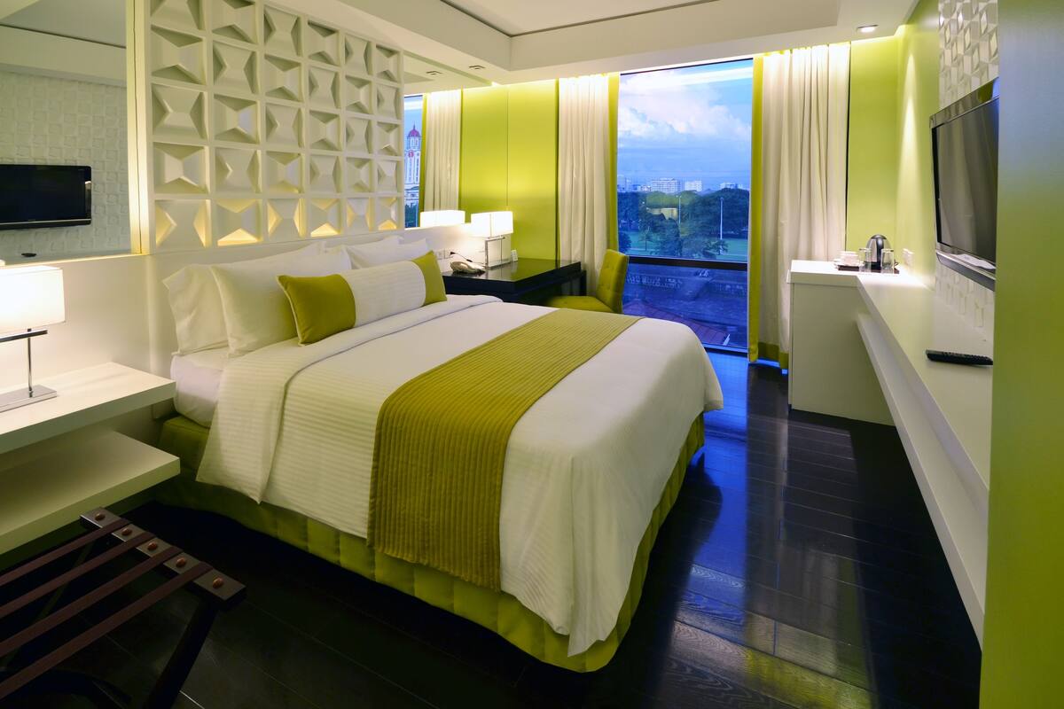 Ein modernes Hotelzimmer mit einem großen Bett, einem Schreibtisch, einem Fernseher und einem Balkon mit Blick auf die Stadt.