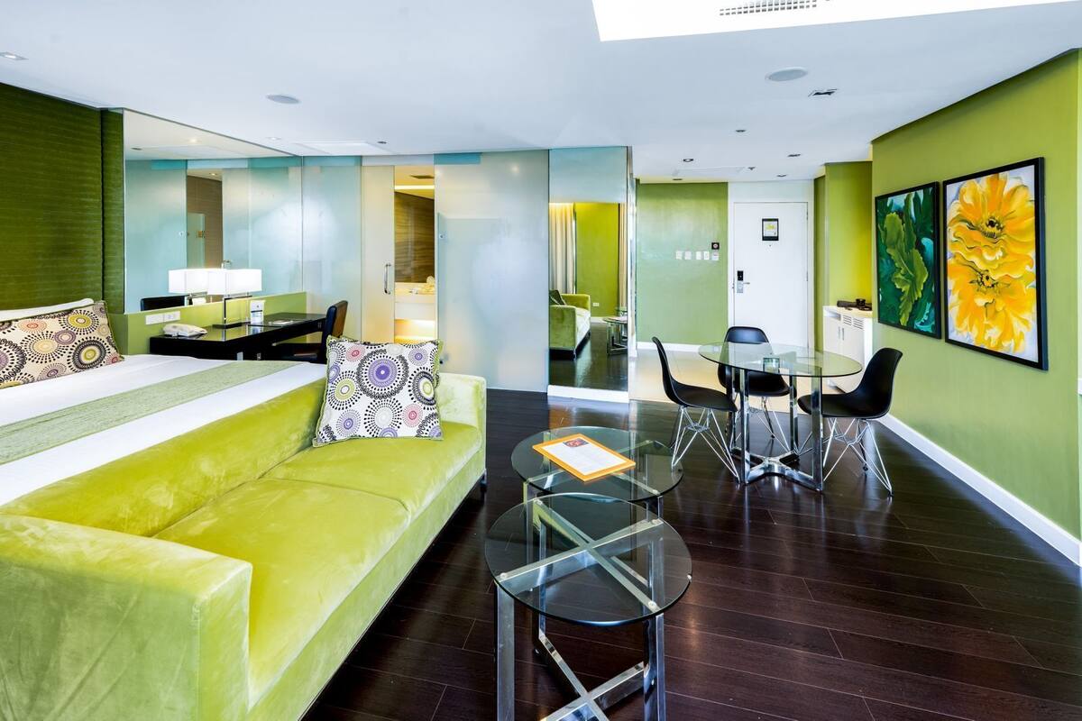 Ein modernes Hotelzimmer mit einem grünen Sofa, einem Glastisch und einem Essbereich mit einem Tisch und Stühlen.