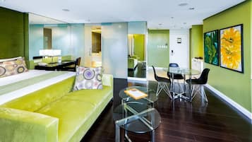 A modern hotel room with a green sofa, a glass coffee table, and a dining area with a glass table and chairs.