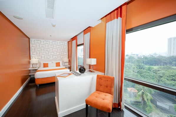 A hotel room with a bed, a desk, a chair, and a large window offering a city view.