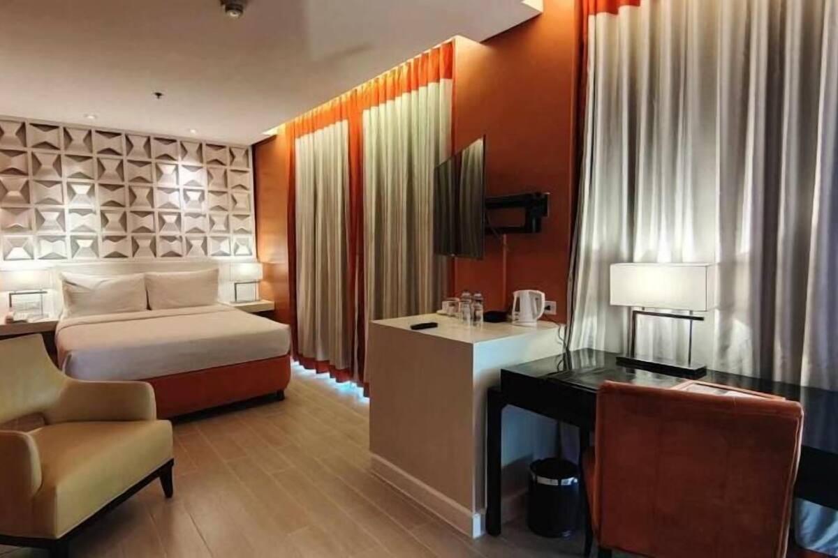 Ein Hotelzimmer mit Bett, Schreibtisch, Stuhl, Fernseher und einer Wand mit geometrischem Muster.