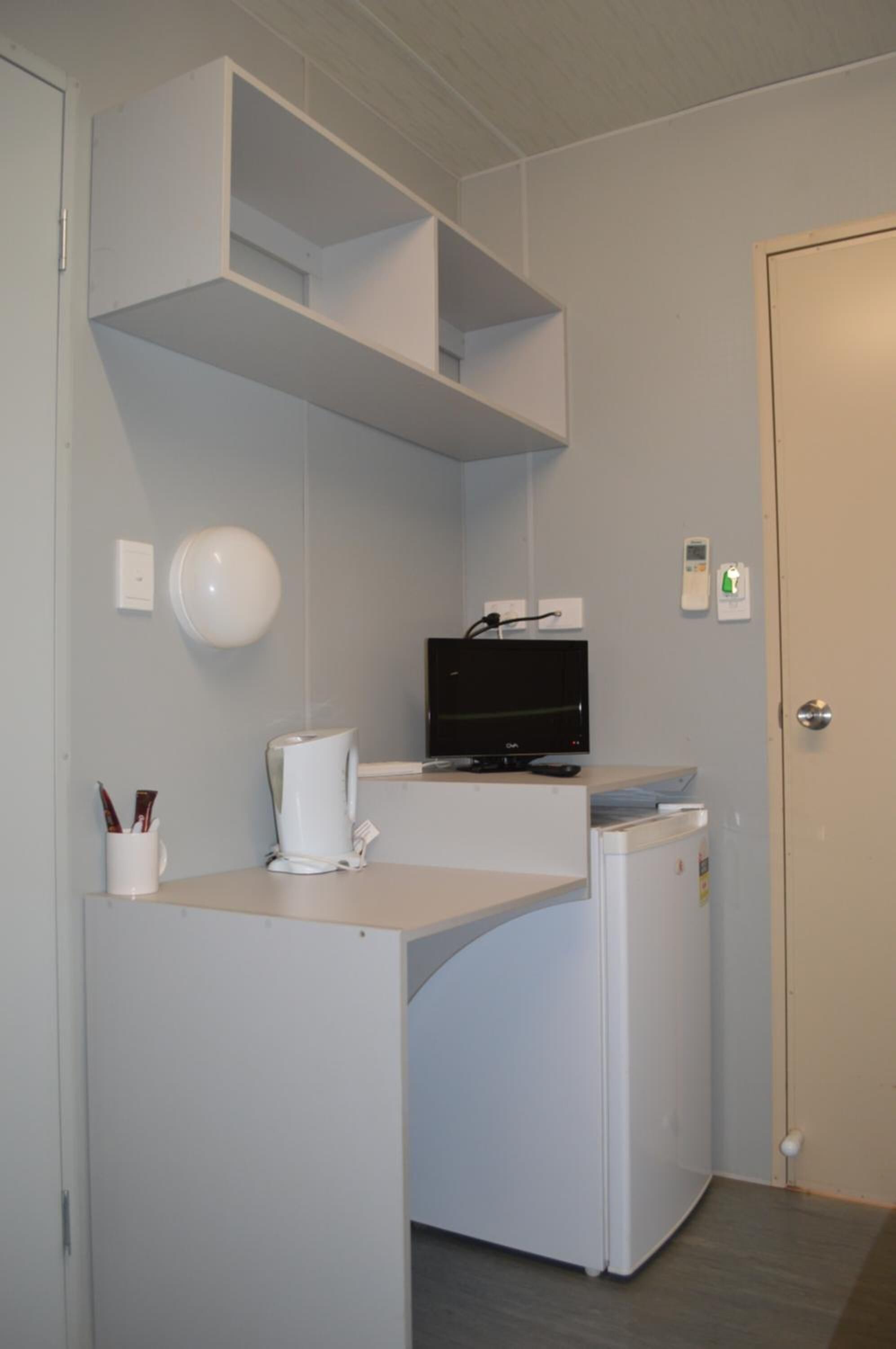 A compact kitchenette with a microwave, coffee maker, and a flat-screen TV on a white countertop.
