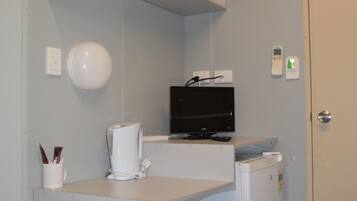 A compact kitchenette with a microwave, coffee maker, and a flat-screen TV on a white countertop.