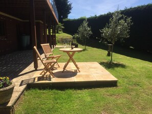 An outdoor patio with a table and chairs, a small garden area, and a hedge in the background. - Riverdown B&B (Exeter)