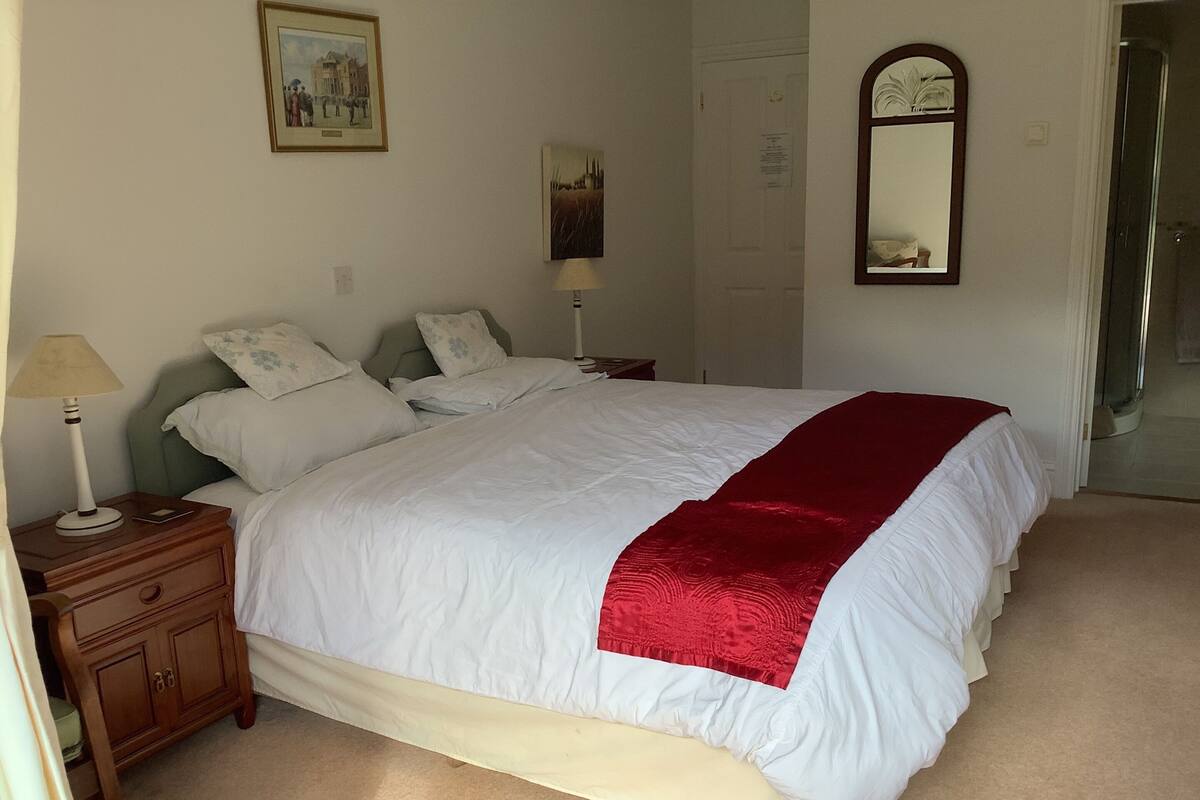 A neatly made bed with a red blanket, a bedside lamp, a wooden nightstand, and a mirror on the wall.