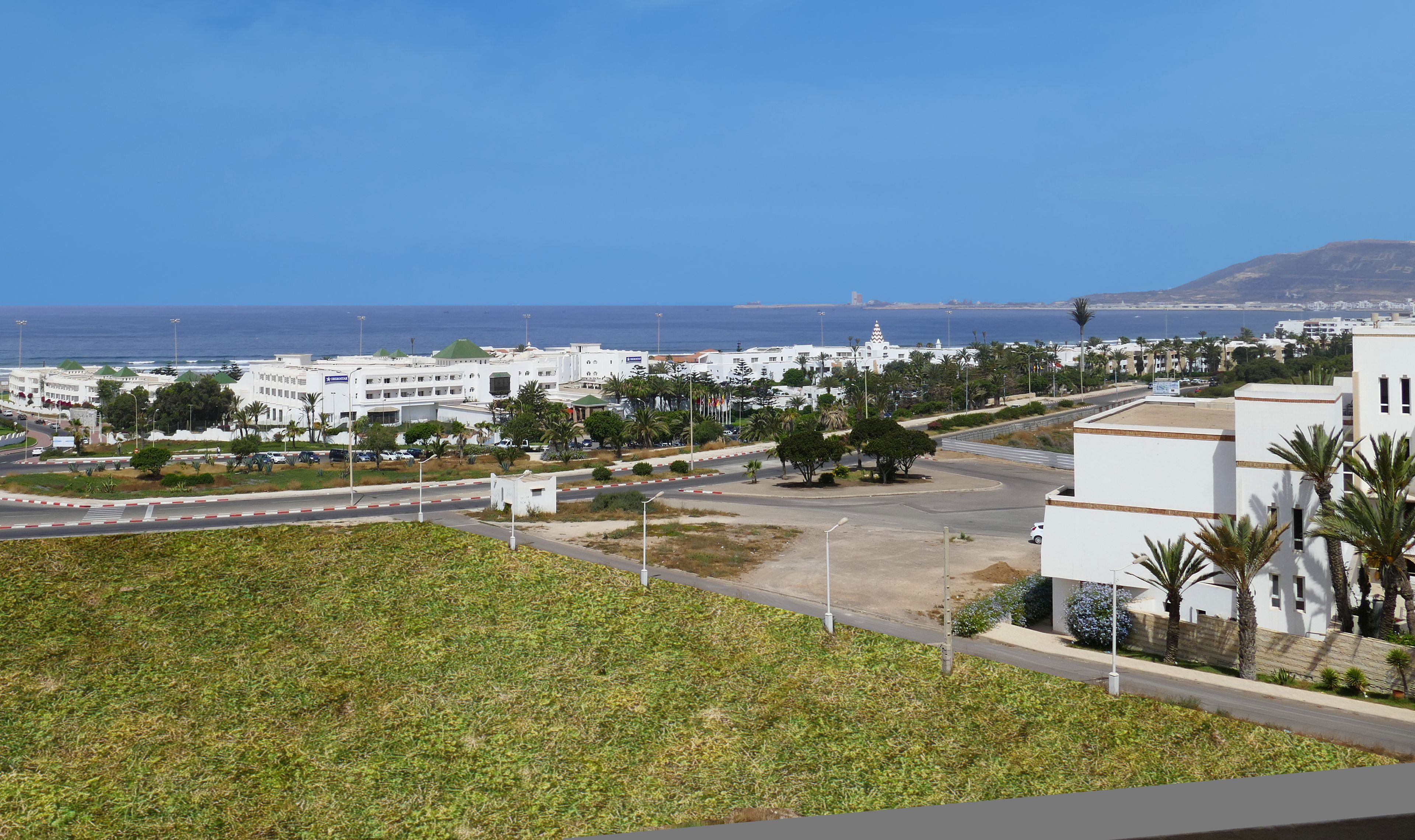 A coastal cityscape with white buildings, a clear blue sky, and a view of the sea.