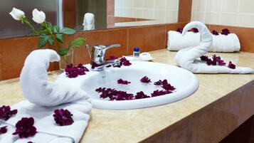 A bathroom with a sink, white towels, and purple flowers.