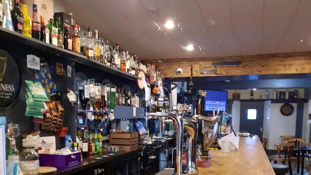 Zona de bar con mostrador de madera, estantes llenos de botellas, dispensador de gel hidroalcohólico y un dardo en la pared.
