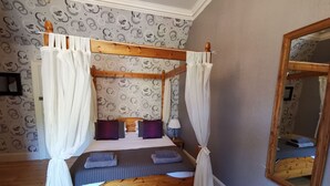 Una cama con dosel y cortinas blancas, cabecera de madera y papel tapiz estampado.
