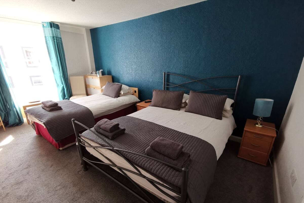 Una habitación de hotel con dos camas, una mesita de noche, una lámpara y una ventana con cortinas.