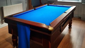 Una mesa de billar en una habitación con piso de madera, una ventana con vistas y un techo con iluminación por rieles.