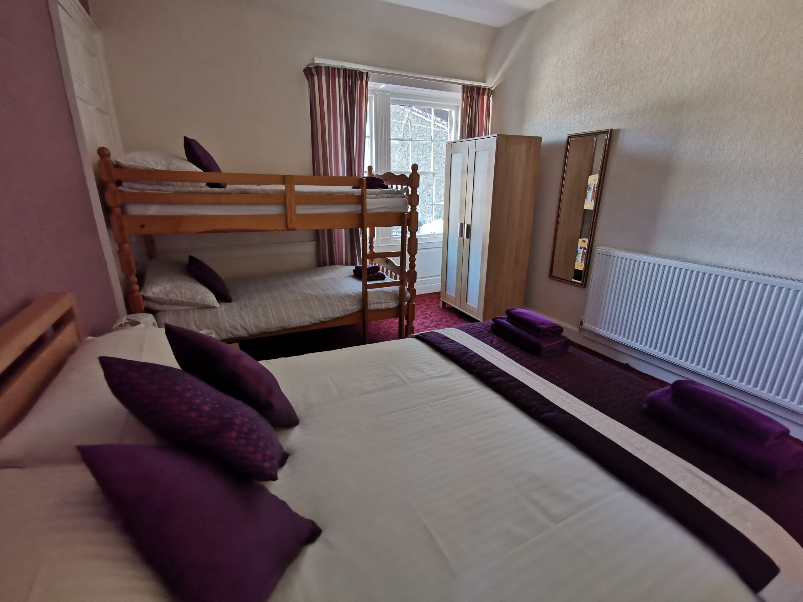 A room with bunk beds, a wardrobe, a mirror, and a radiator.