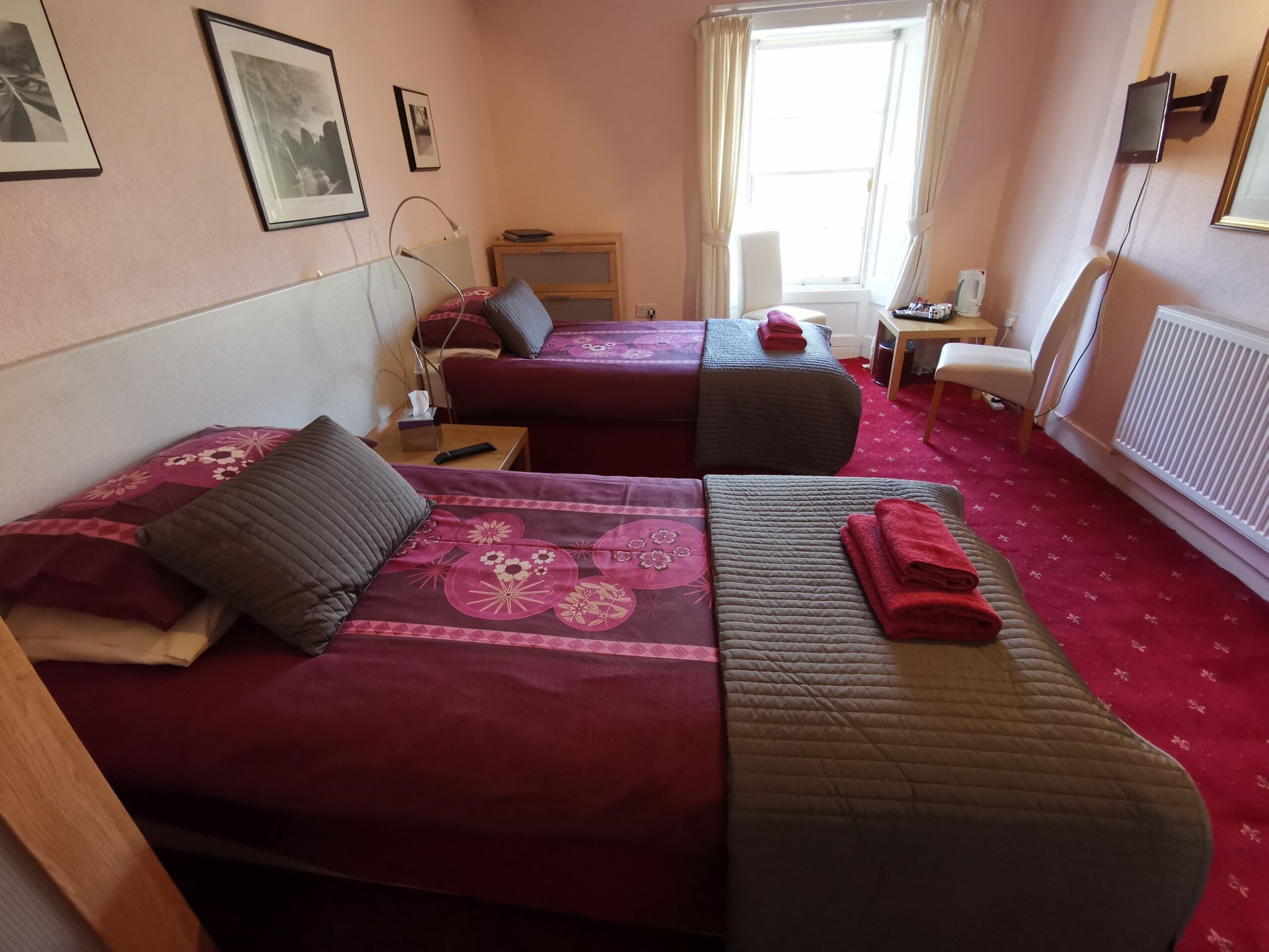 Une chambre avec deux lits, une petite table, une chaise et un radiateur.