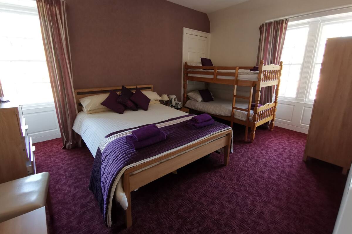 Habitación de hotel con una cama grande, una cama individual, una cama nido de madera y un escritorio con una silla.