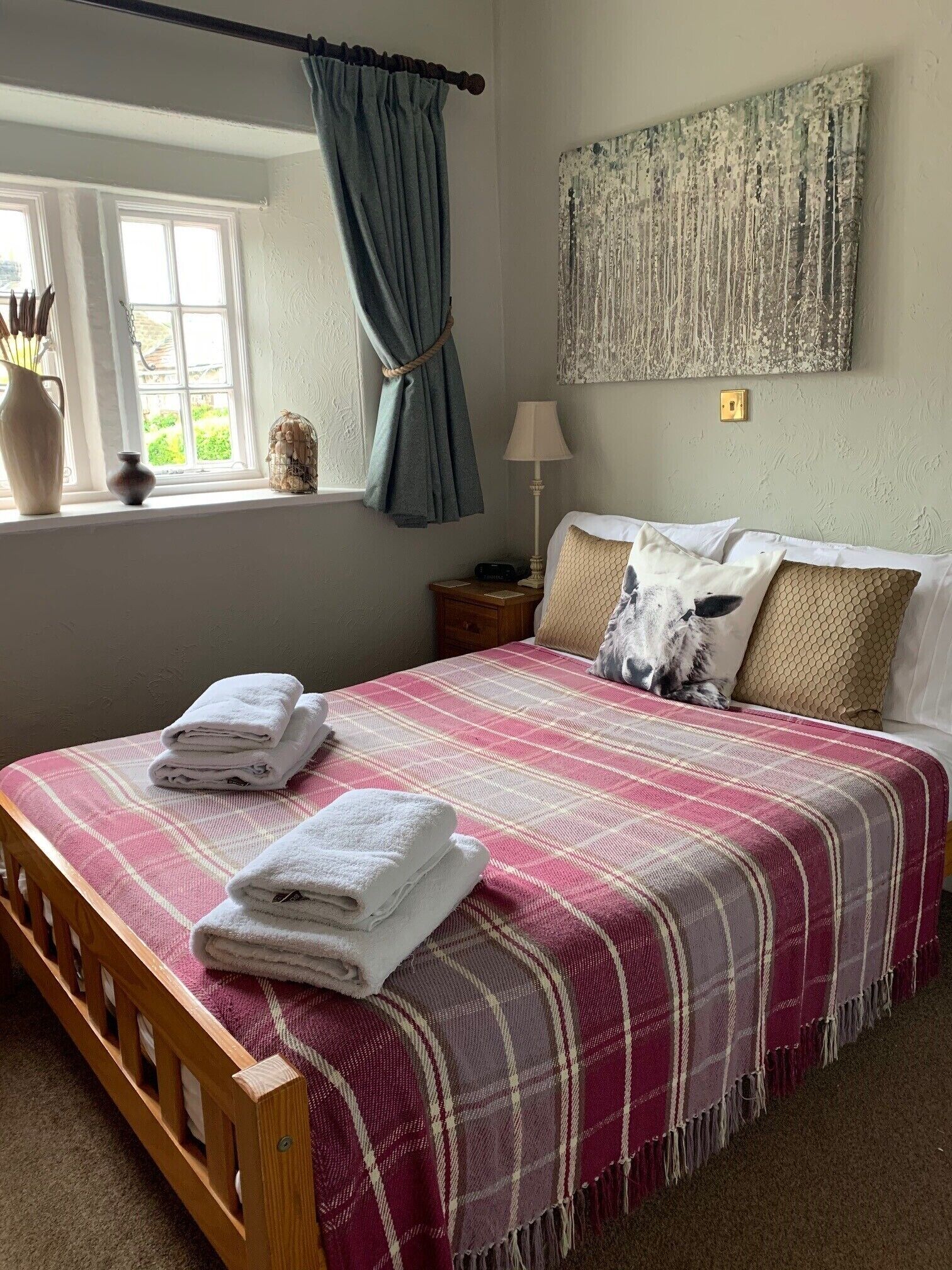 A neatly made bed with a plaid bedspread, a bedside lamp, and a window with curtains.