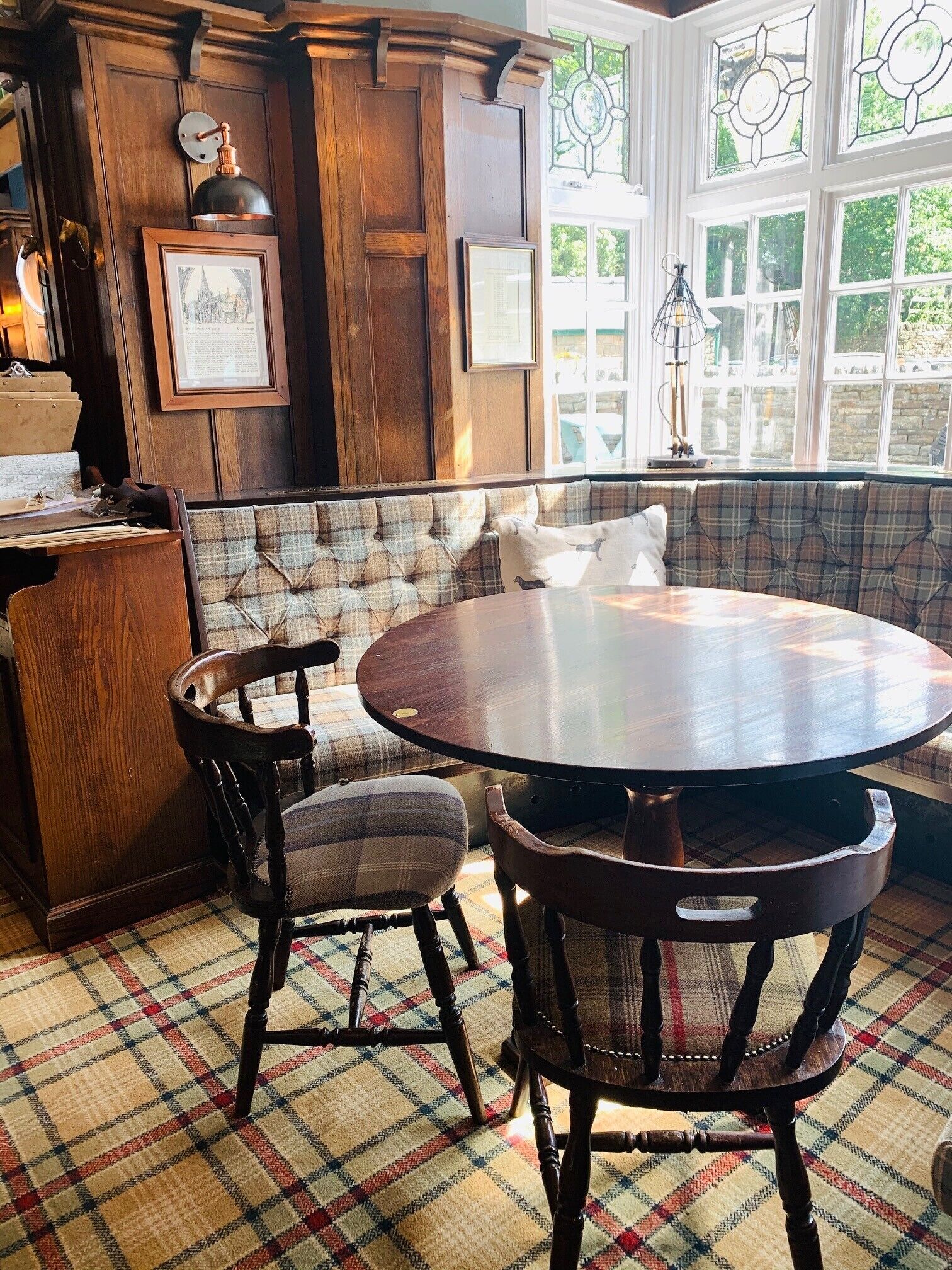 A cozy dining area with a round table, wooden chairs, and a plaid-patterned bench.