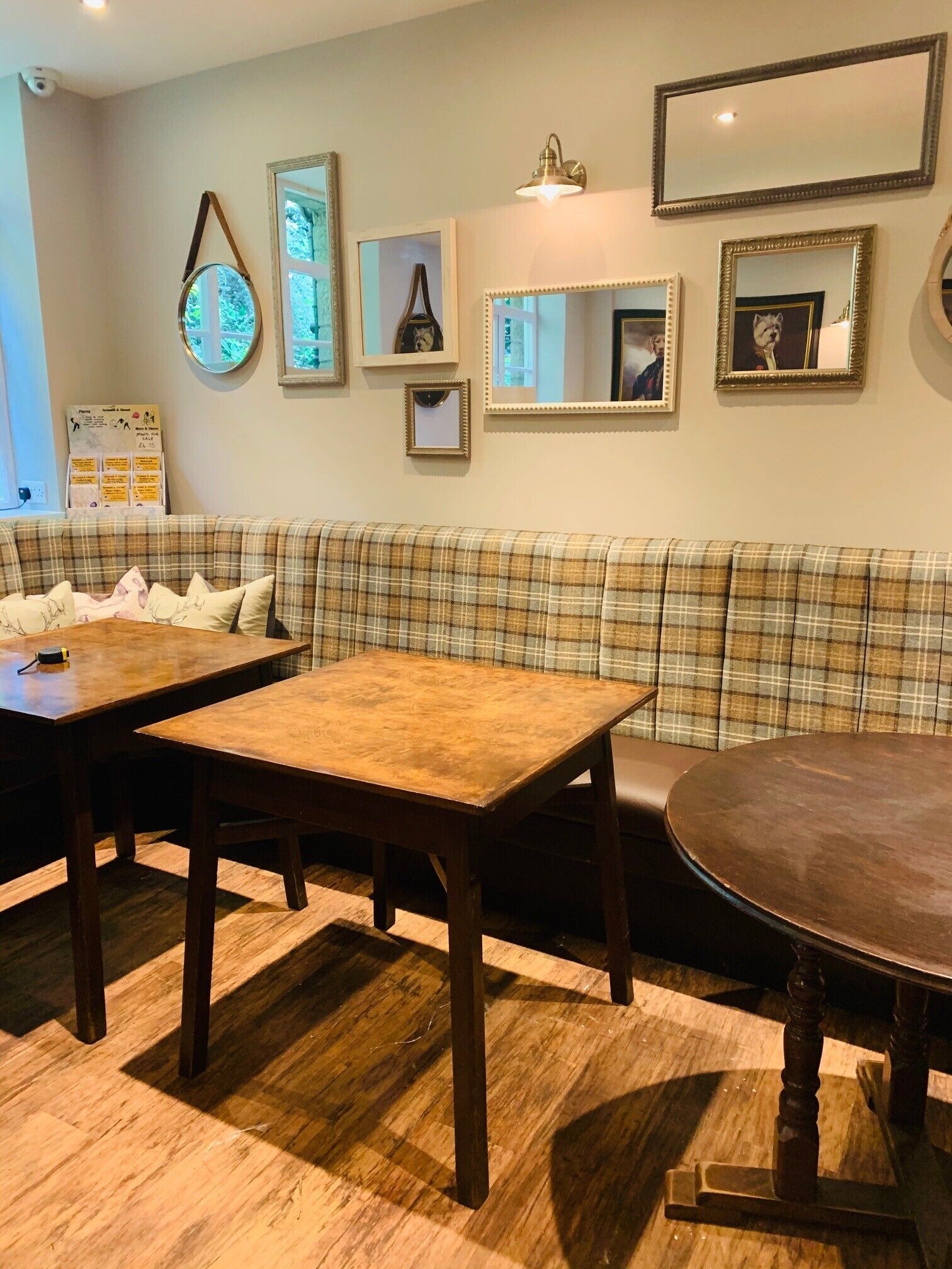 A cozy dining area with a plaid sofa, wooden tables, and a variety of framed pictures on the wall.
