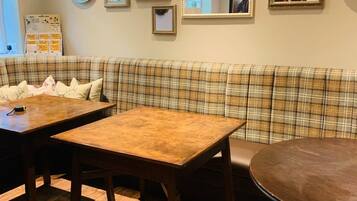 A cozy dining area with a plaid sofa, wooden tables, and a variety of framed pictures on the wall.