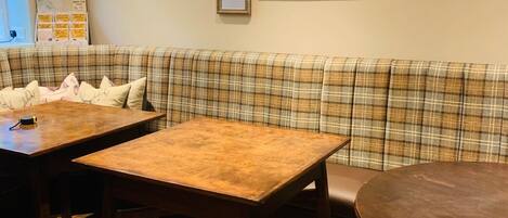A cozy dining area with a plaid sofa, wooden tables, and a variety of framed pictures on the wall.