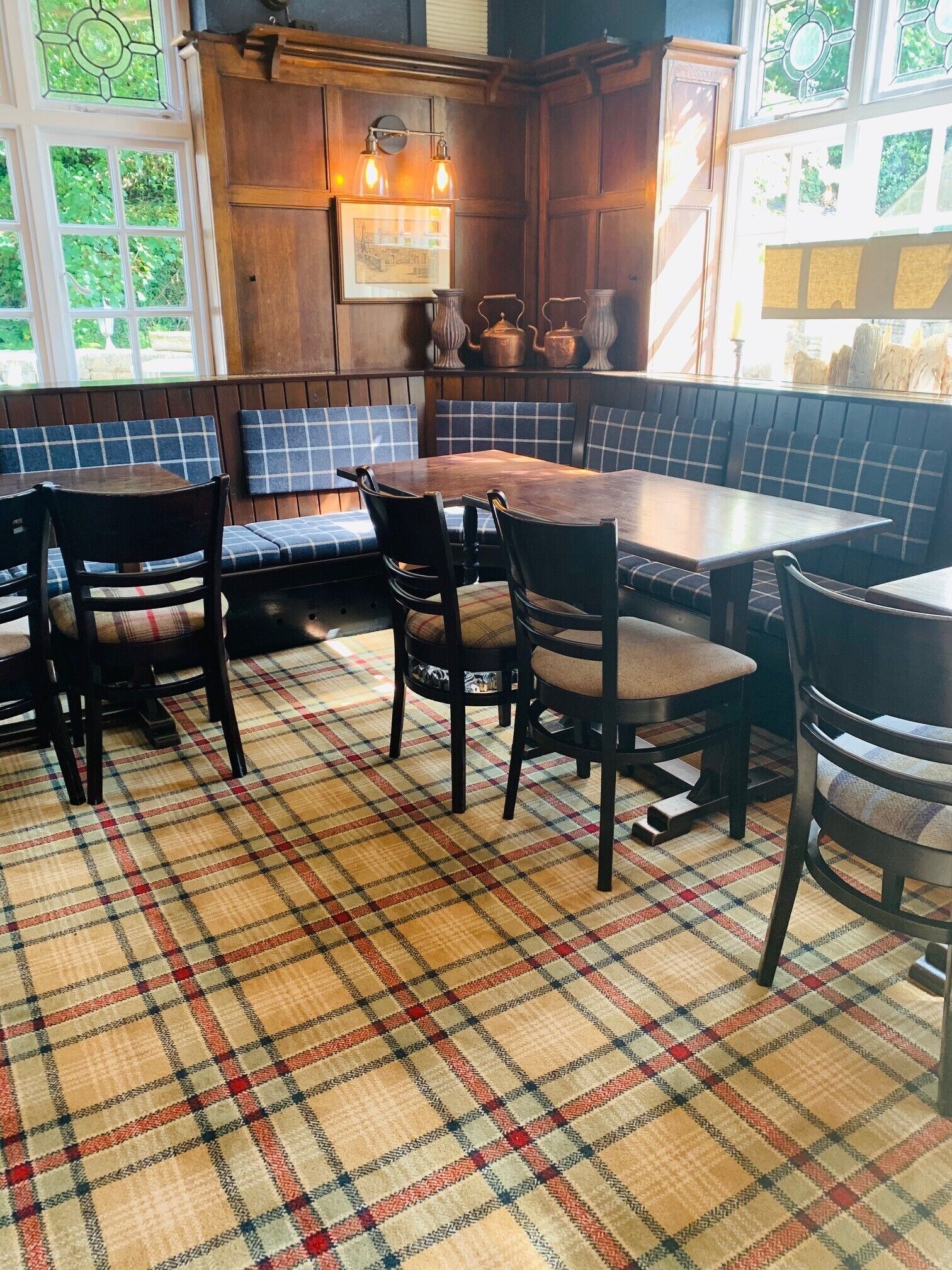 Um restaurante com chão quadriculado, mobiliário de madeira e vista para o verde através de grandes janelas.