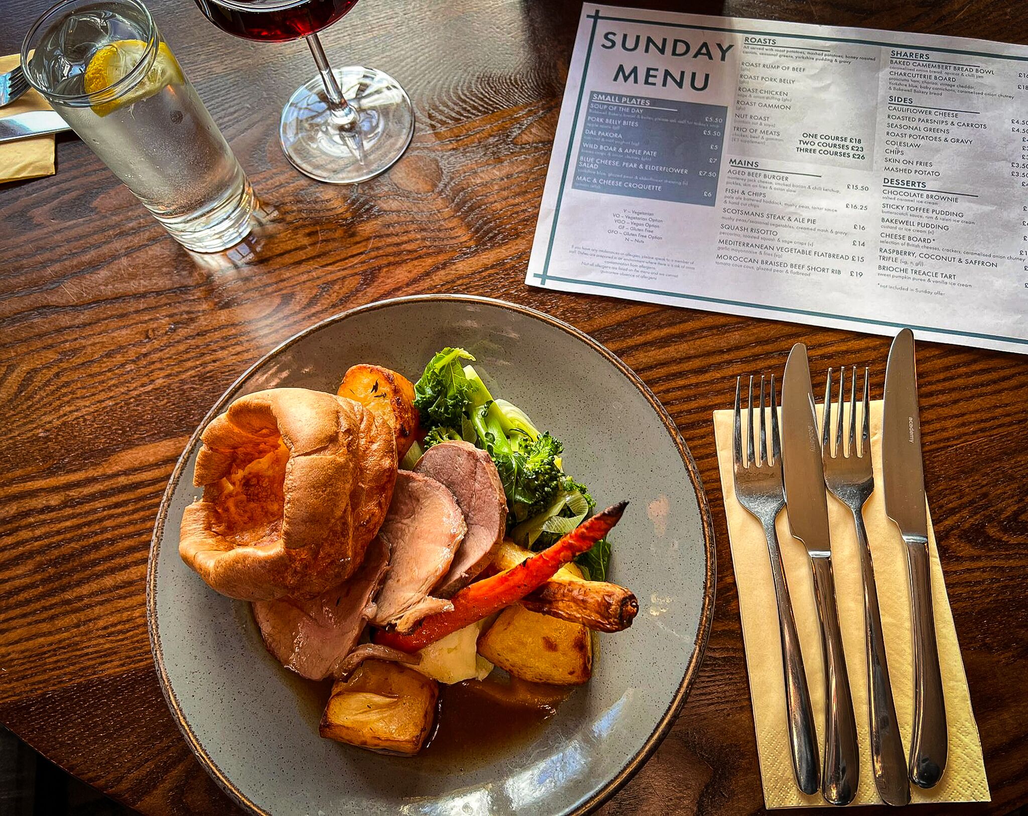 A plate of food with roast beef, vegetables, and Yorkshire pudding on a table with a menu and cutlery.