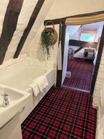 A bathroom with a white bathtub, a white sink, and a red plaid floor. There is a hanging plant and a small table with a lamp.