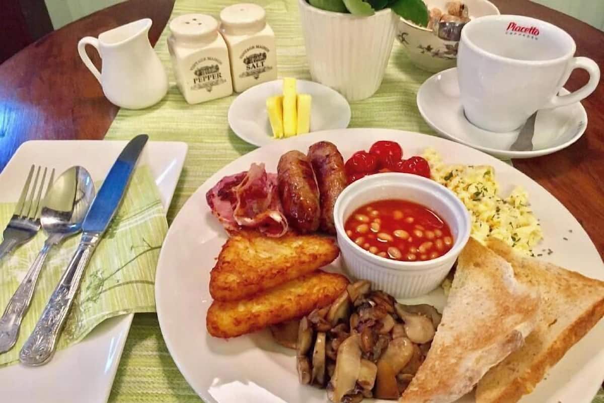 Prato de café da manhã com torradas, feijão, linguiça, cogumelos e ovos.
