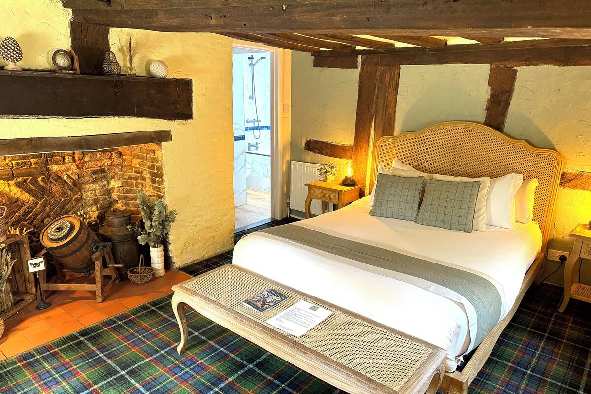 Quarto tradicional com cama, um banco de madeira, lareira e parede de pedra.