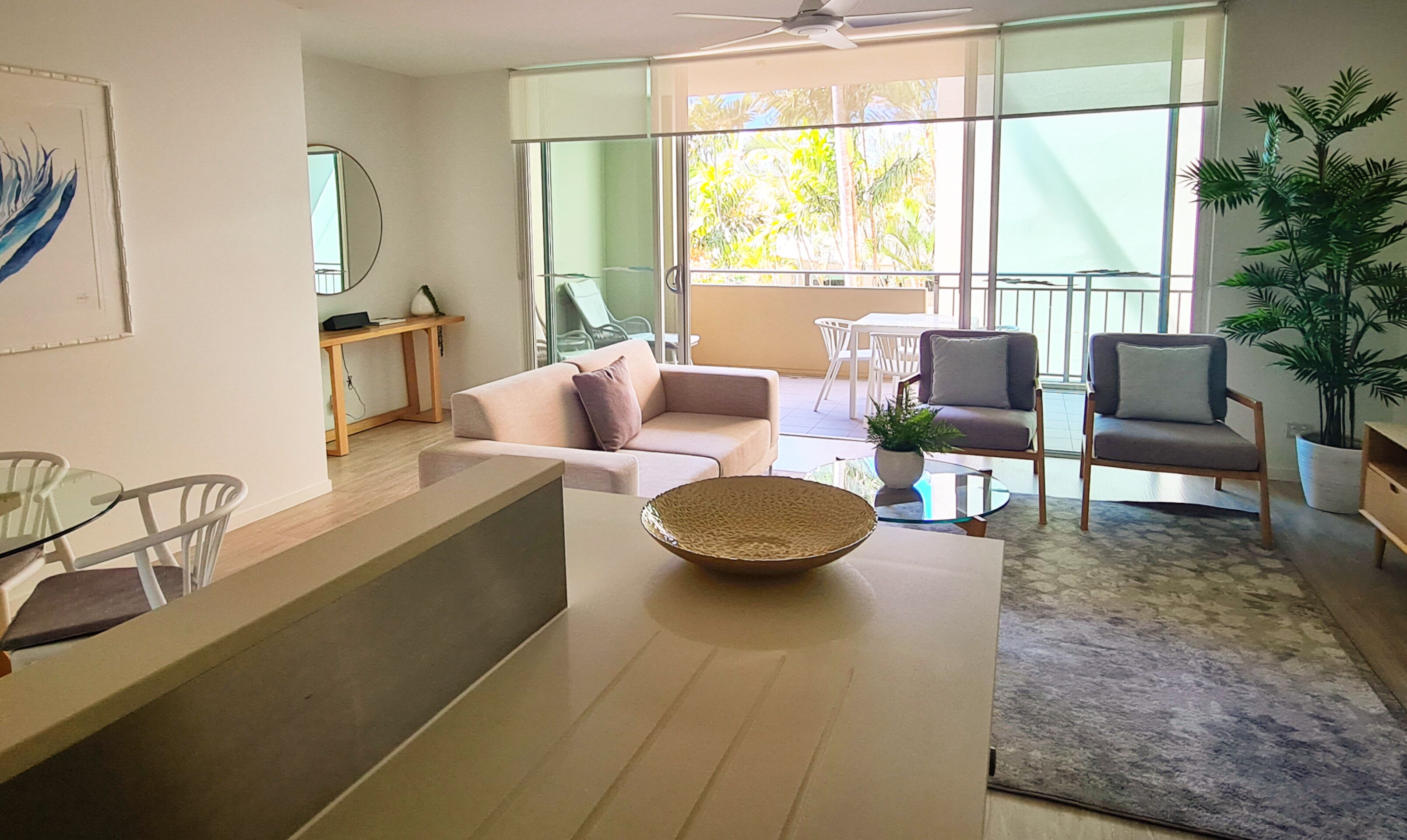 Un salon moderne avec un canapé, des fauteuils, une table basse et un balcon offrant une vue sur la verdure.