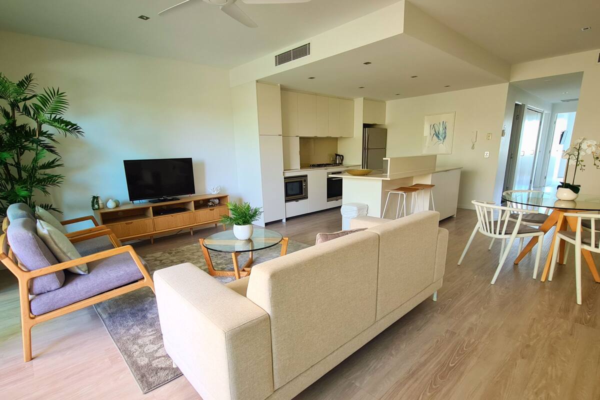 A modern living room with a sofa, a TV, and a dining area with chairs and a table.