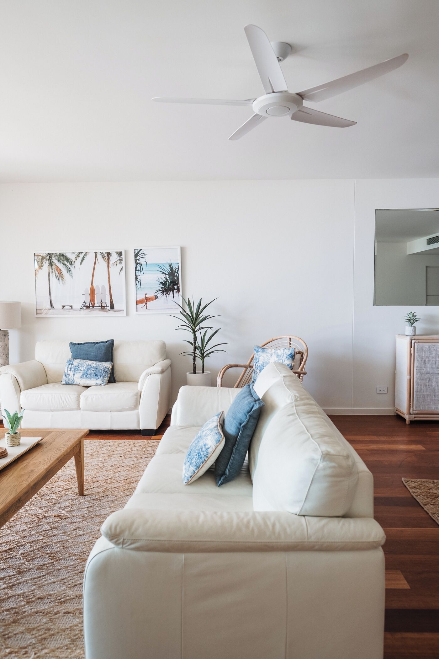 A living room with a white sofa, a wooden coffee table, a ceiling fan, and two wall-mounted paintings.