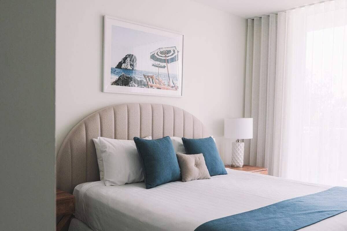 A neatly made bed with a headboard, a bedside lamp, and a framed picture on the wall.