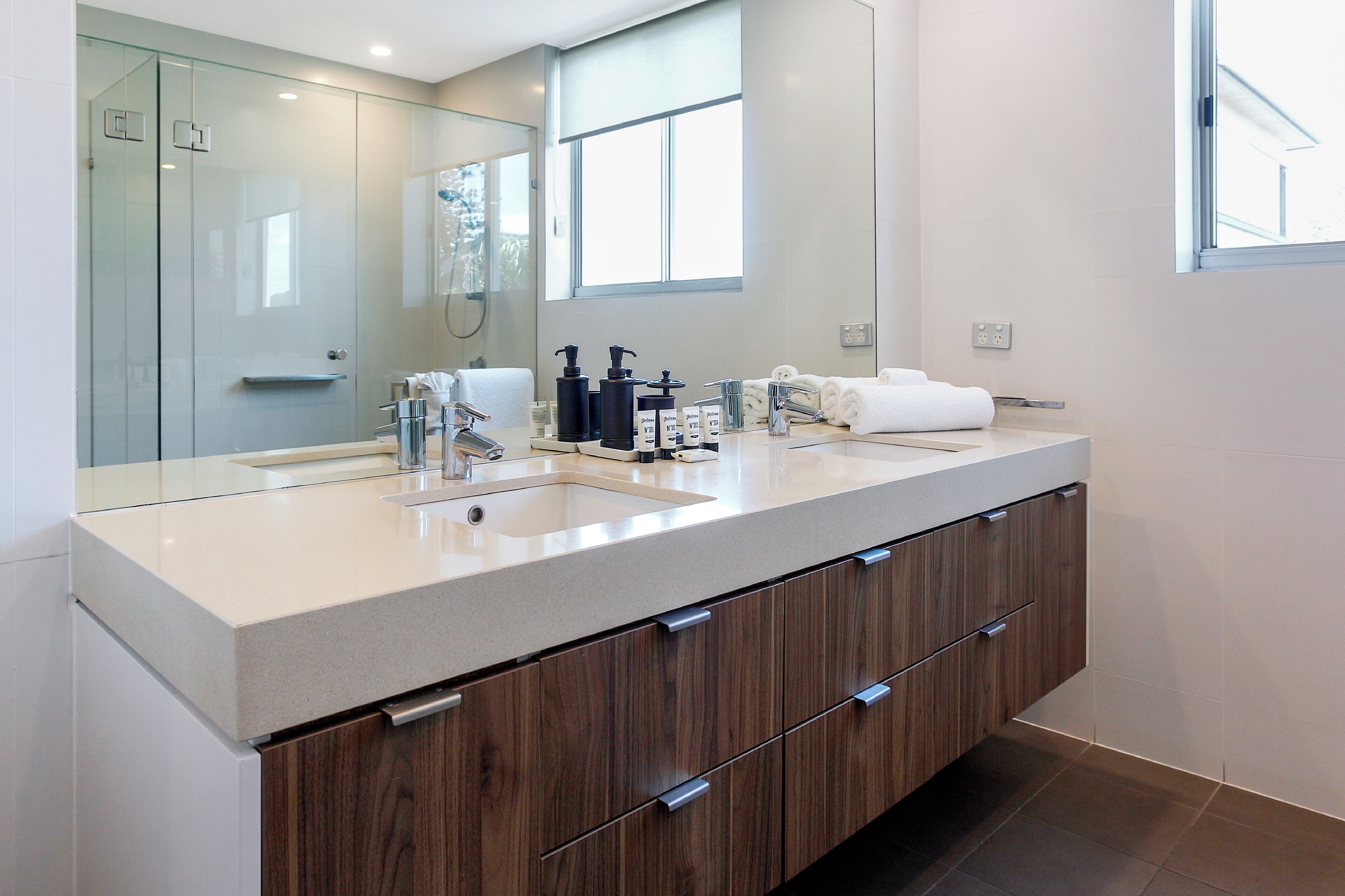 Une salle de bain moderne dotée d’un grand miroir, d’un double vasque, de meubles en bois et d’une cabine de douche en verre.