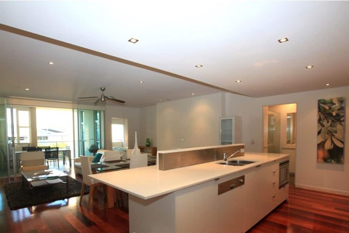 A modern kitchen with a central island, a dining area with a sofa and chairs, and a large window providing natural light.