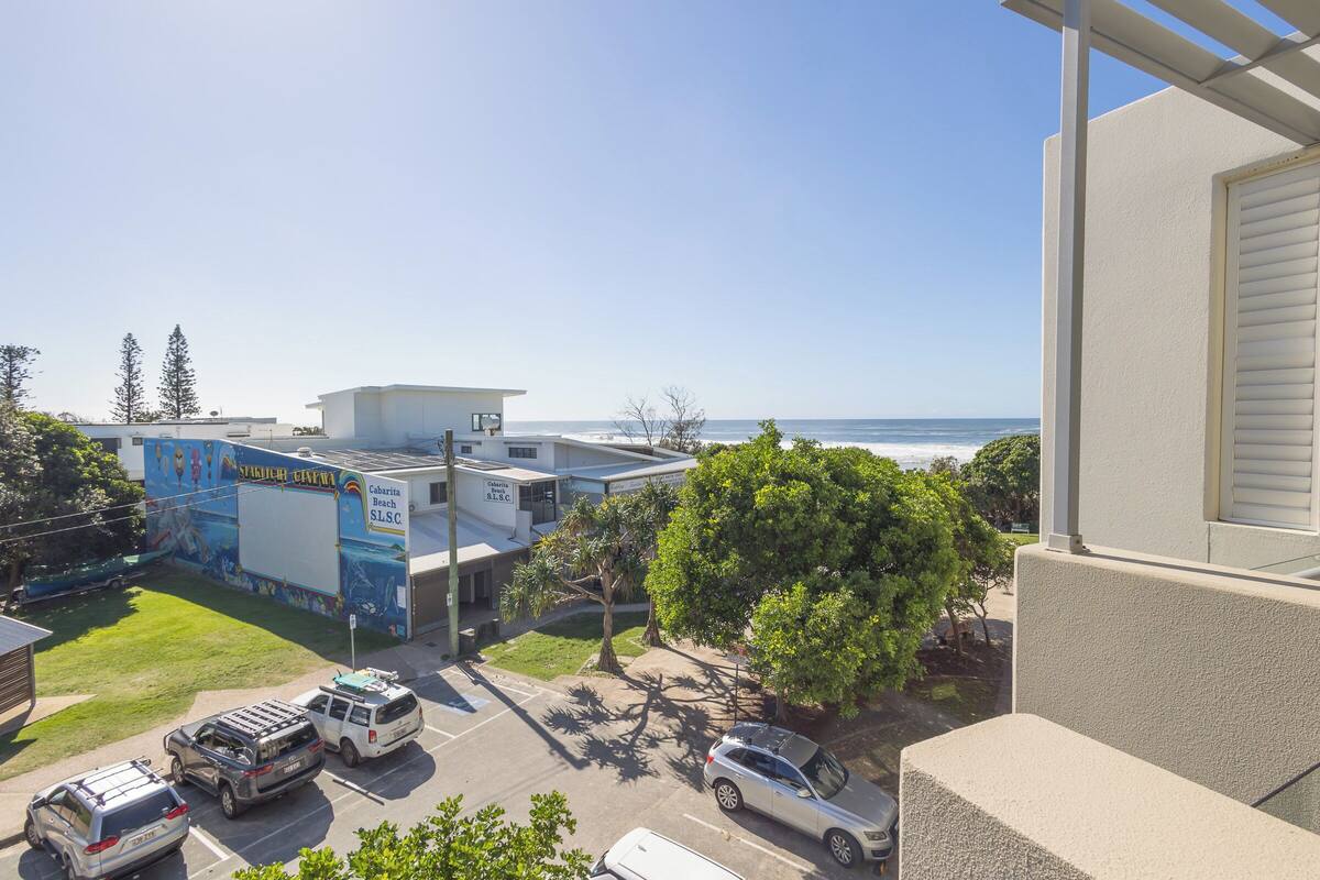 A parking lot with several vehicles, a building with a mural, and a view of the ocean.