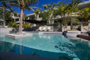 A swimming pool with lounge chairs and palm trees, surrounded by a modern building with balconies.