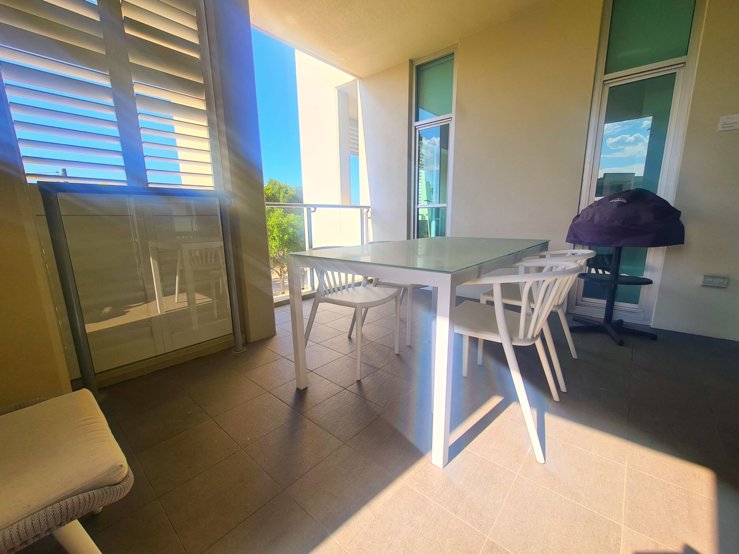 Ein Balkon mit Glastisch und Stühlen, einem violetten Sonnenschirm und Blick auf den Himmel.