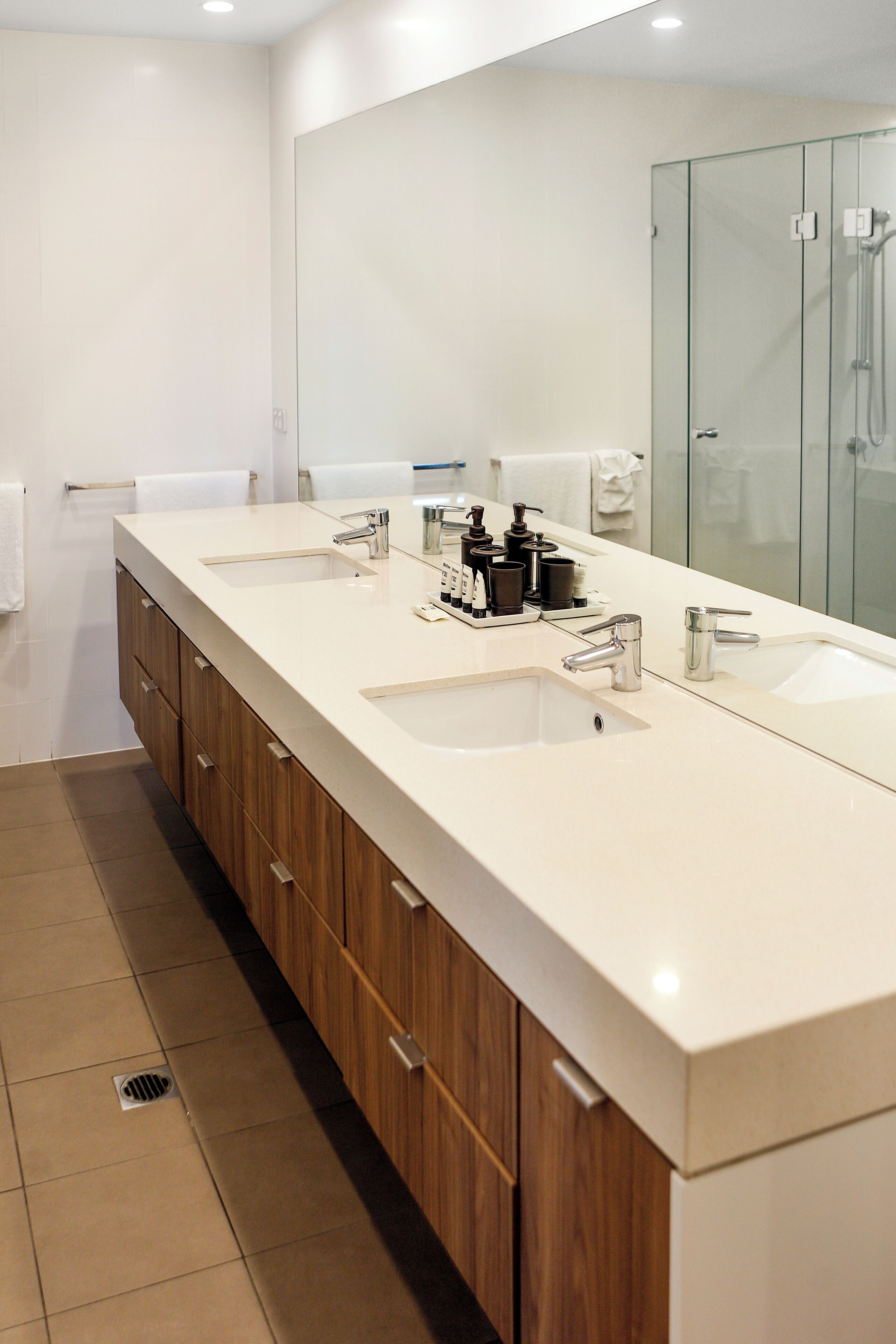 Un baño moderno con un mueble de tocador espacioso, dos lavamanos y una cabina de ducha de vidrio.