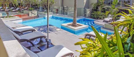 A pool area with lounge chairs and umbrellas, surrounded by greenery.