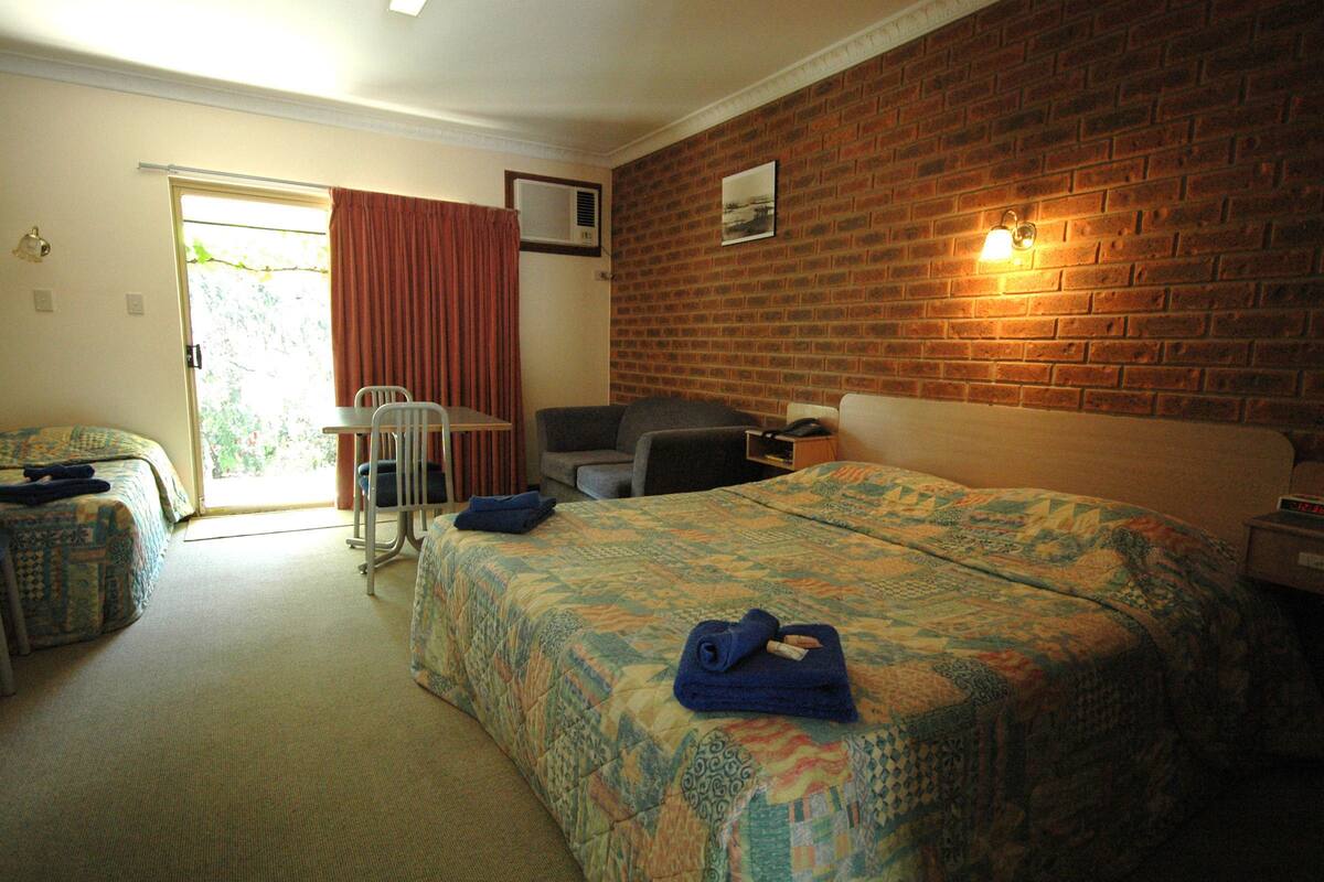 Habitación de hotel con una cama grande, un escritorio, una silla y vistas al exterior a través de una puerta corrediza.