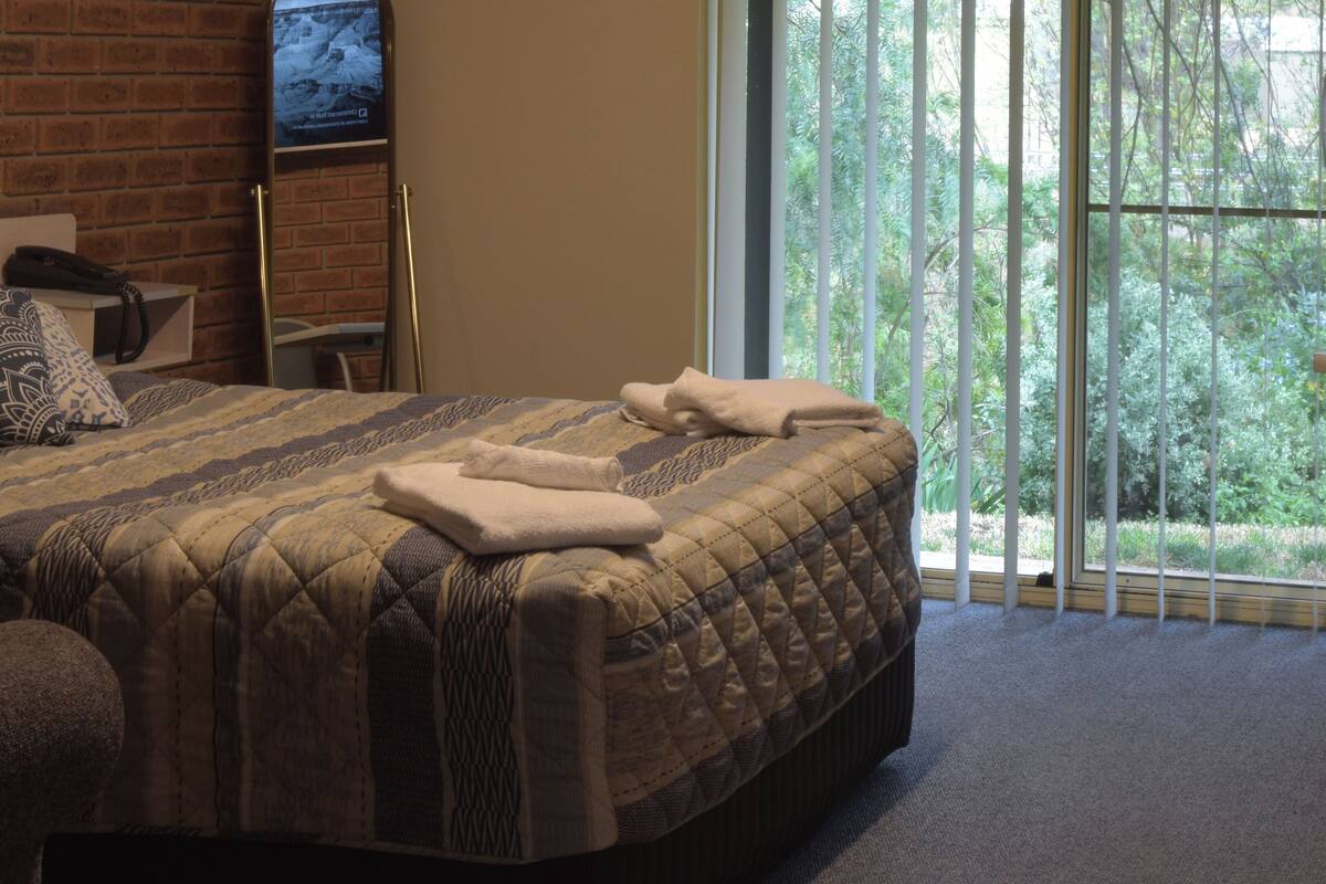 Habitación de hotel con una cama grande, un escritorio y vistas a zonas verdes por la ventana.