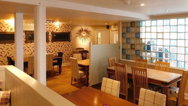 A dining area with a wooden table and chairs, a patterned wall, and a large window with multiple panes. - The Nags Head (Norwich)