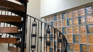 A spiral staircase with wooden steps and black balusters, leading to a room with a large window featuring a mosaic pattern. - The Nags Head (Norwich)