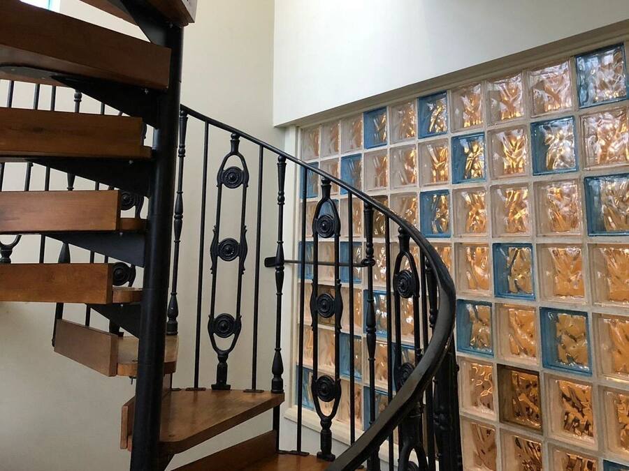 A spiral staircase with wooden steps and black balusters, leading to a room with a large window featuring a mosaic pattern.
