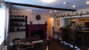 A cozy living room with a fireplace, a dining area, and a bar with various bottles and glasses. - The Nags Head (Norwich)