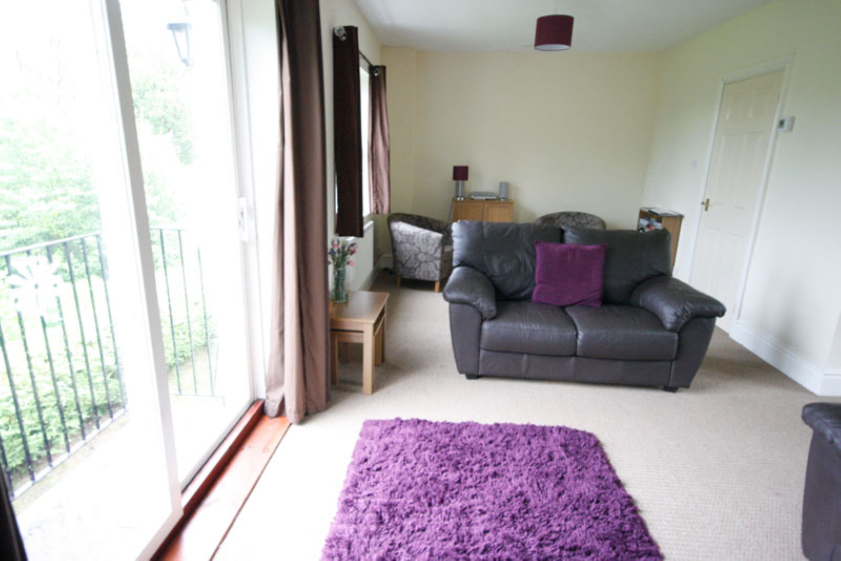 A living room with a grey sofa, a purple rug, and a wooden side table.